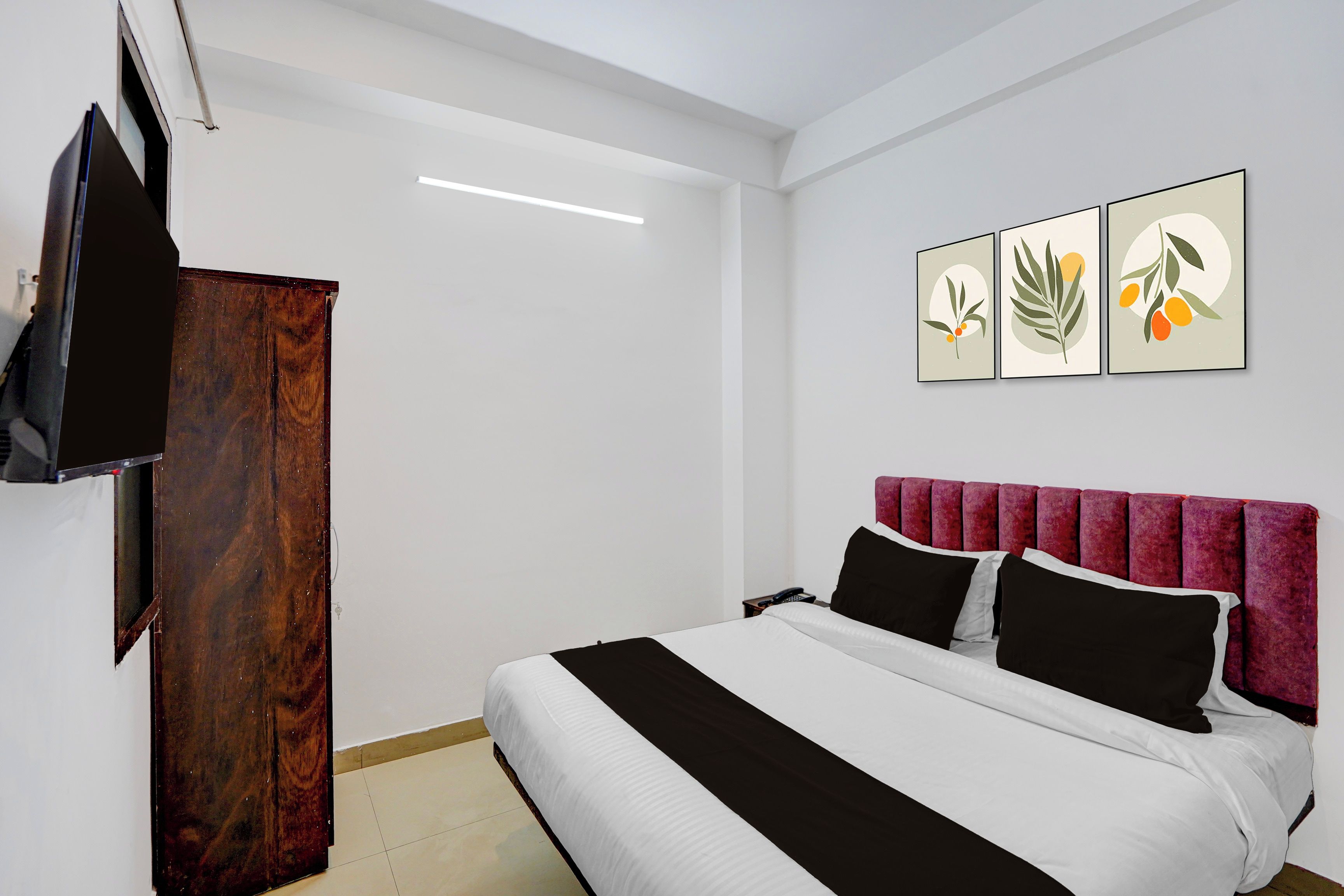A hotel room with a bed, a television, a wardrobe, and three framed pictures on the wall.