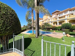 A well-maintained pool area with a clear blue pool, surrounded by neatly trimmed grass and palm trees. - Holiday Home in Nerja With Sea Views (Nerja)