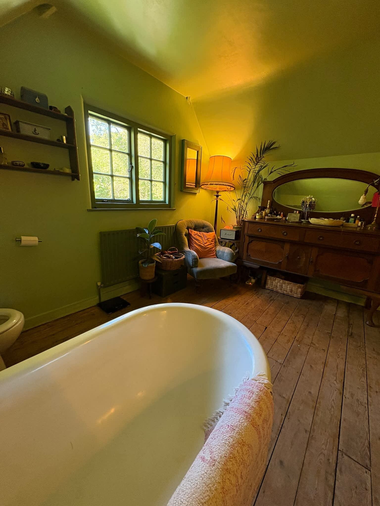 Un bagno con vasca, pavimento in legno, finestra, termosifone e mobile lavabo con specchio.