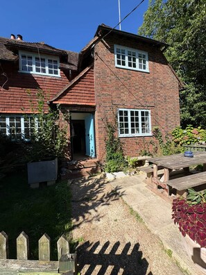 A two-story brick house with a front door, a small porch, and a garden area with a wooden fence. - Two bed home with garden & parking in Bramley, Surrey Hills (Bramley)