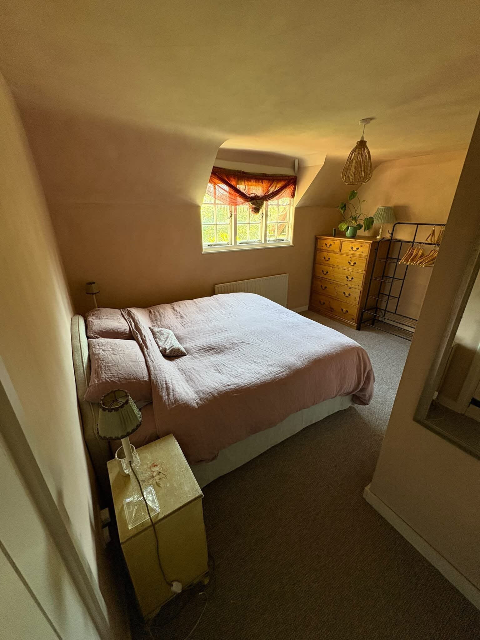 Ein Schlafzimmer mit einem Einzelbett, einem Schminktisch, einem Fenster mit Vorhängen und einer Pendelleuchte.