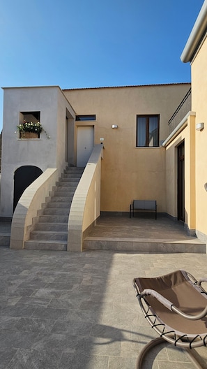 Ein Gebäude mit einer Treppe, die zu einer Tür führt, einer Bank und einem überdachten Sitzbereich.