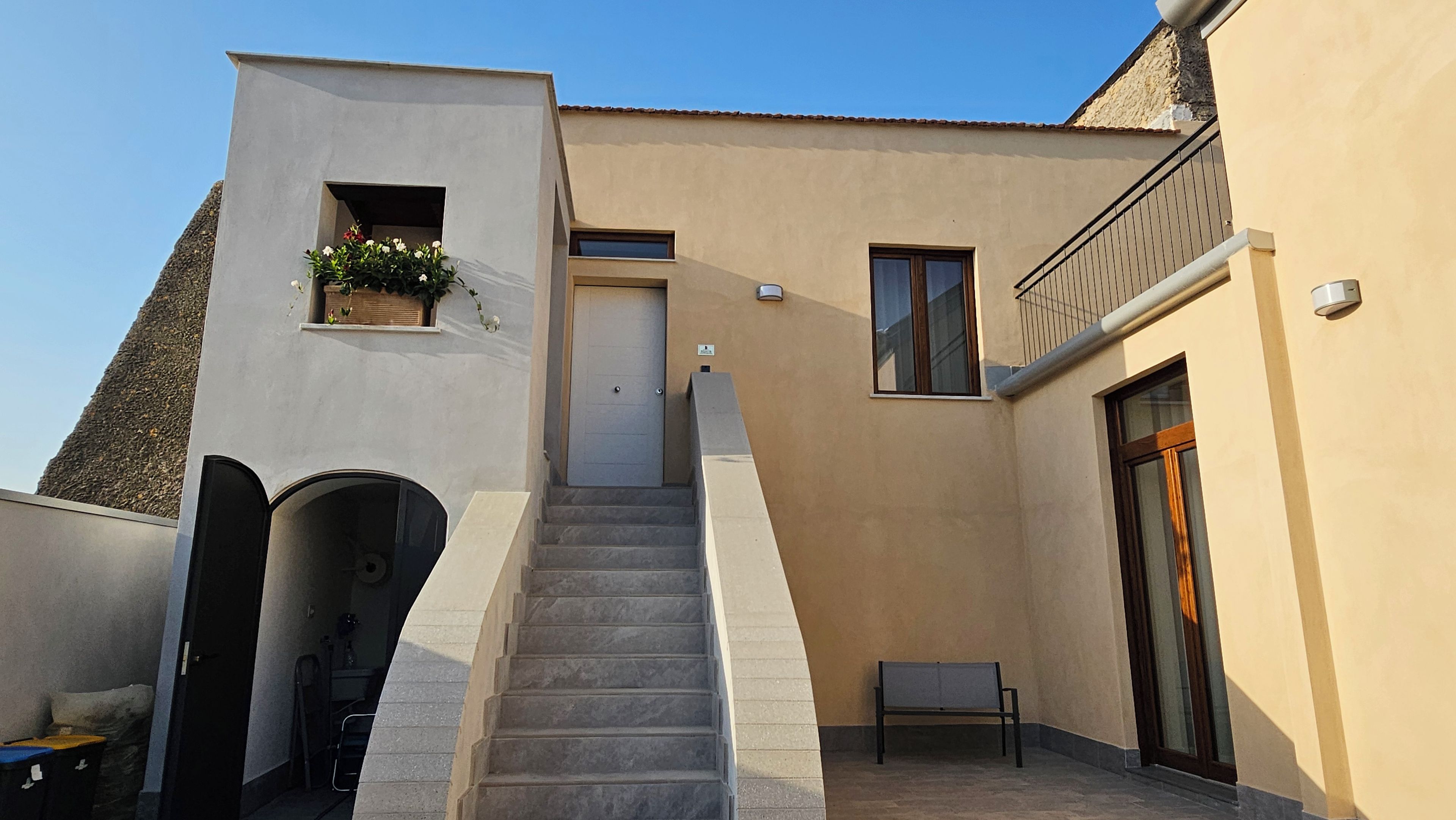 Un edificio con una escalera que lleva a una puerta, un banco pequeño y una ventana.