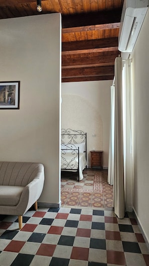 A room with a bed, a nightstand, a sofa, and a patterned floor.