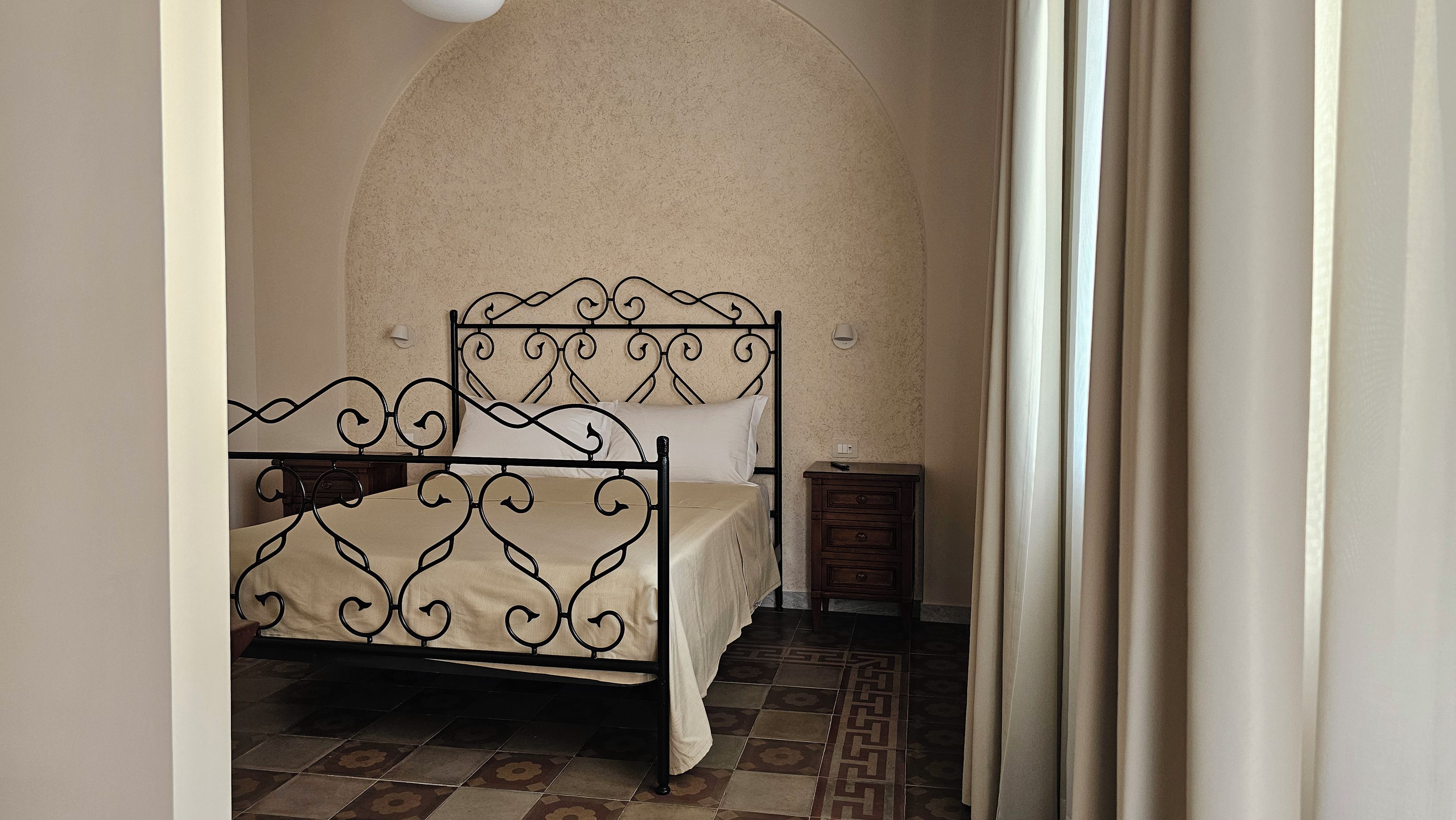 A bedroom with a bed, a nightstand, and a wall-mounted light fixture.