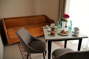 Una habitación con un sofá, una mesa de comedor con platos de comida, tazas y un jarrón con flores.