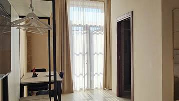 A spacious room with a high ceiling, a dining area with a table and chairs, and a large window with curtains.