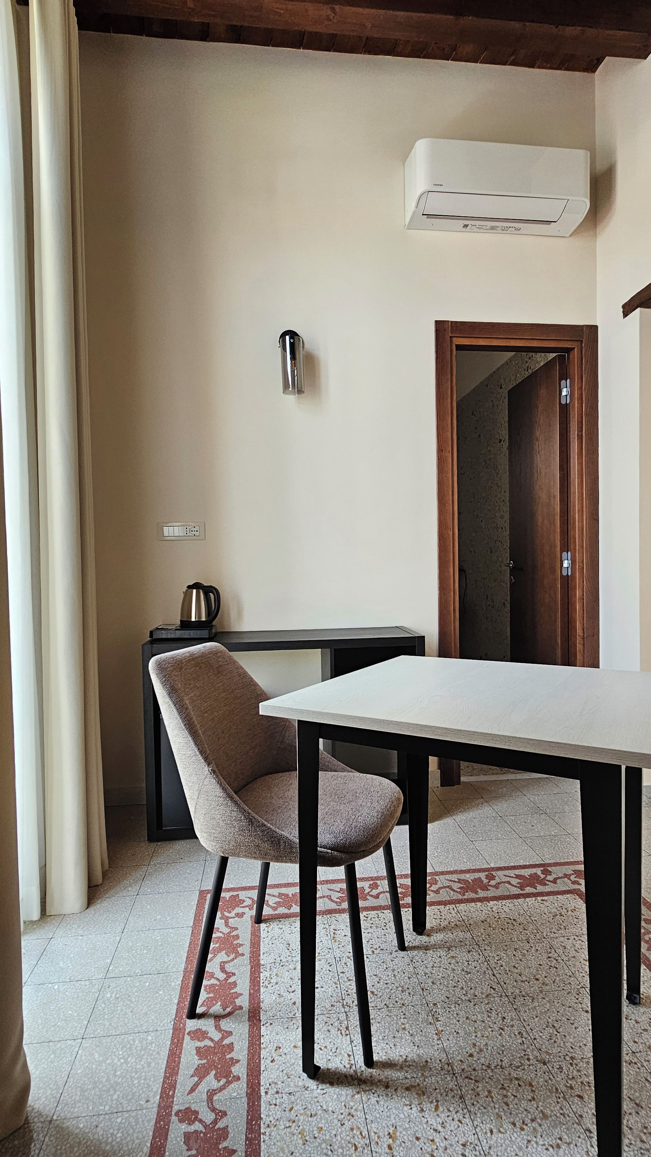 A room with a table, a chair, a coffee maker, and a door leading to another room.