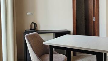 A room with a table, a chair, a coffee maker, and a door leading to another room.