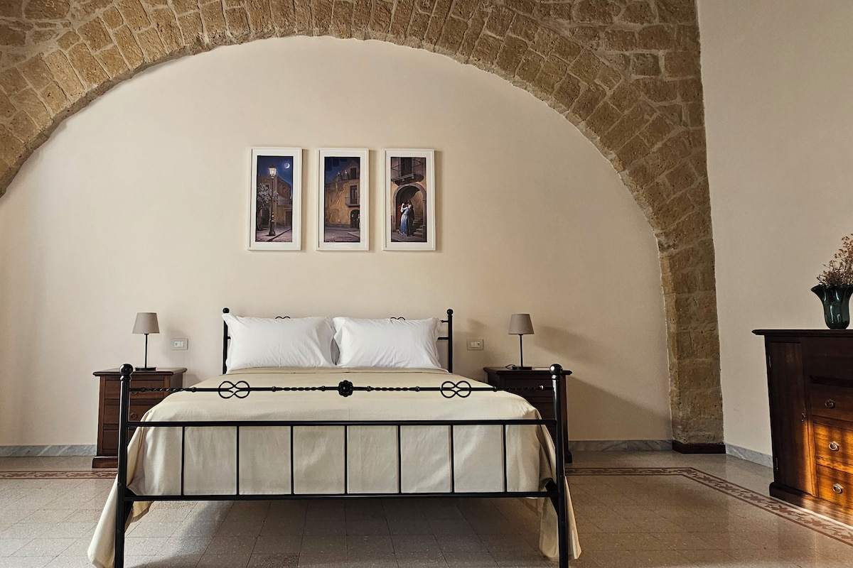 Ein Schlafzimmer mit einem Steingewölbe, einem Bett mit Metallgestell, zwei Nachttischen mit Lampen und drei gerahmten Bildern an der Wand.