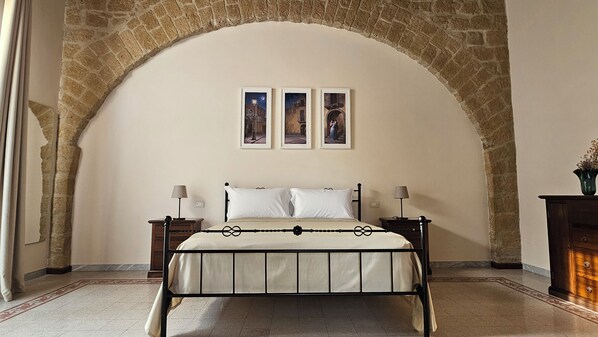A bedroom with a stone arch, a bed with a metal frame, two bedside tables with lamps, and three framed pictures on the wall.