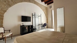 Una habitación de hotel con un arco de piedra, una cama, un televisor, un escritorio con una silla y un armario.