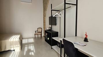 Una habitación pequeña y bien iluminada con una cama, un escritorio, una silla y un televisor.