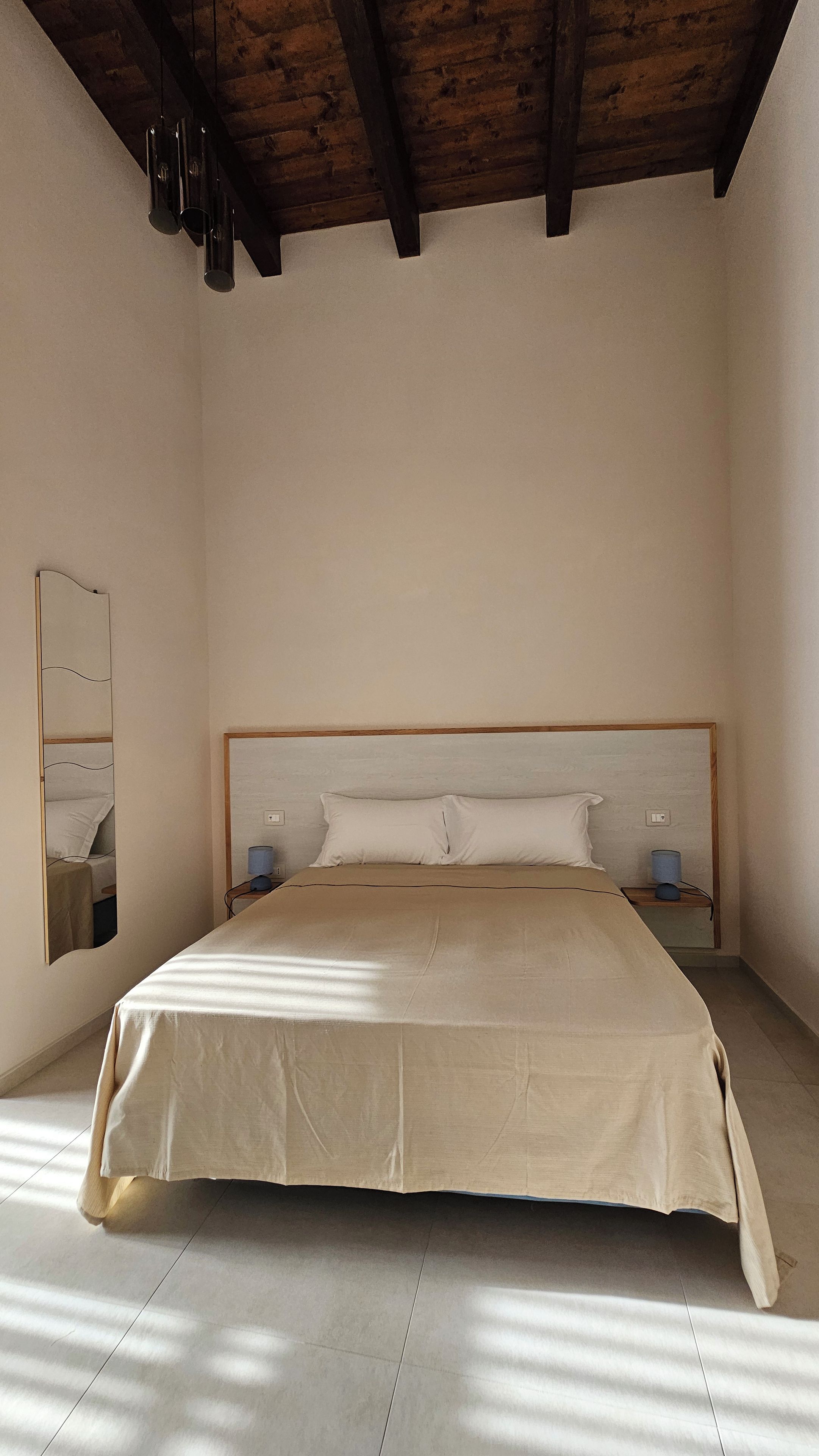 A bedroom with a large bed, a wooden ceiling, and a mirror on the wall.