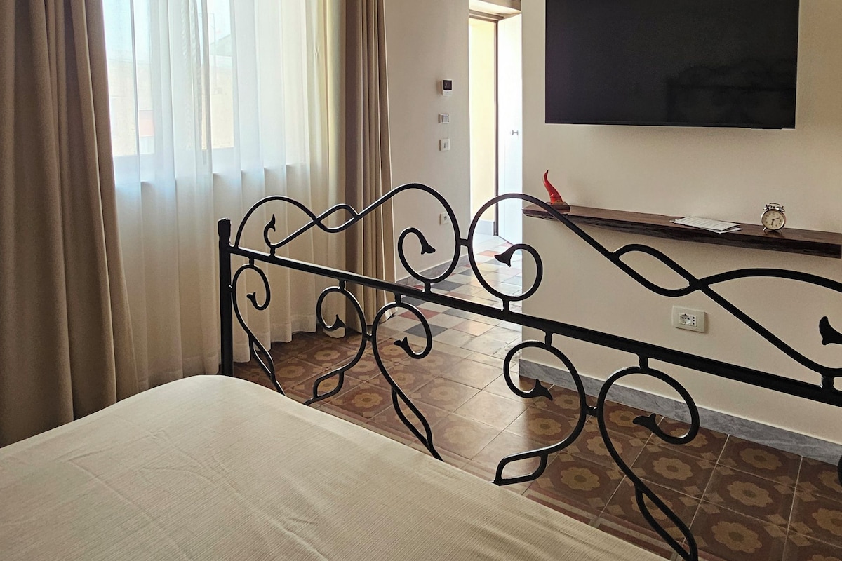 A bedroom with a bed, a TV mounted on the wall, a ceiling fan, and a window with curtains.