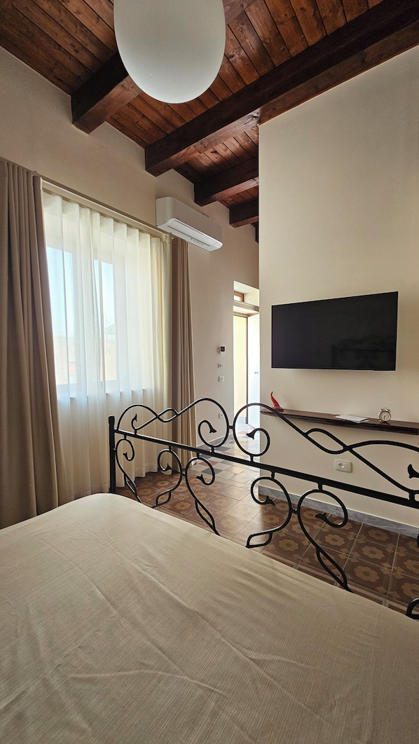 A bedroom with a bed, a TV mounted on the wall, a ceiling fan, and a window with curtains.