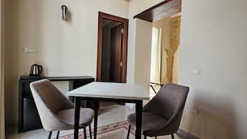 A small dining area with a table and two chairs, a kettle on a table, and a door leading to another room.