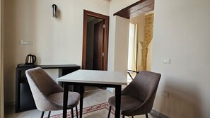 A small dining area with a table and two chairs, a kettle on a table, and a door leading to another room.