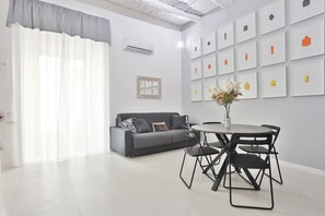 Een moderne woonkamer met een grijze bank, een ronde eettafel met stoelen en een wand met ingelijste kunstwerken.