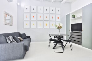 Ein modernes Wohnzimmer mit einem grauen Sofa, einem runden Tisch mit Stühlen und einem Flachbildfernseher auf einem Schrank.