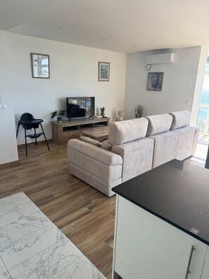 A modern living room with a sofa, TV, and a dining area. - Premium Postiguet Beach Apartments—First-Line Location (Alicante)