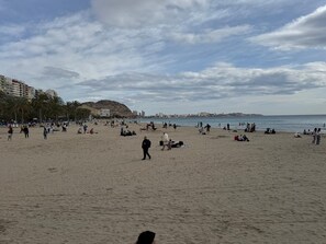 Ein Sandstrand mit Menschen, Palmen und Gebäuden im Hintergrund.
