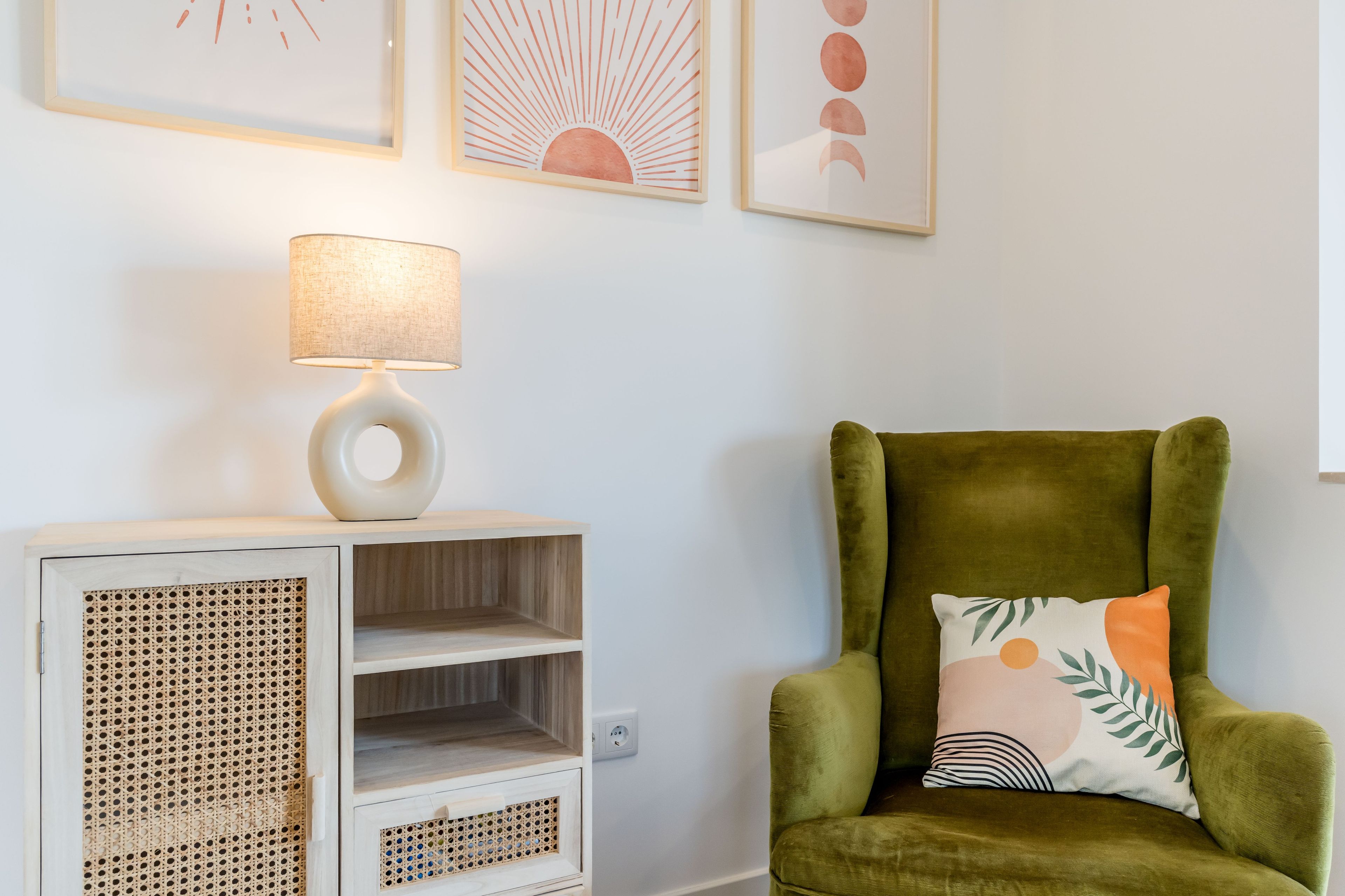 A room with a green armchair, a white side table with a lamp, and a wall with framed artwork.