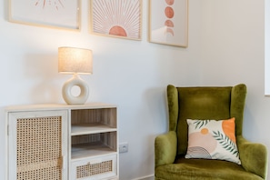 A room with a green armchair, a white side table with a lamp, and a wall with framed artwork. - Villa 'Grandma's Beach' with Sea View, Wi-Fi and Air Conditioning (Albufeira)