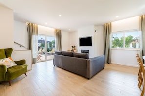A modern living room with a grey sofa, a green armchair, a flat-screen TV, and a sliding glass door leading to an outdoor area. - Villa 'Grandma's Beach' with Sea View, Wi-Fi and Air Conditioning (Albufeira)