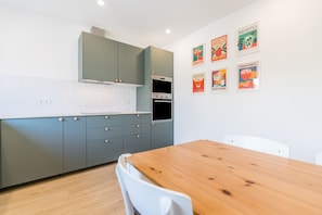 A modern kitchen with grey cabinets, a wooden dining table, and a white chair. There are six framed pictures on the wall. - Villa 'Grandma's Beach' with Sea View, Wi-Fi and Air Conditioning (Albufeira)