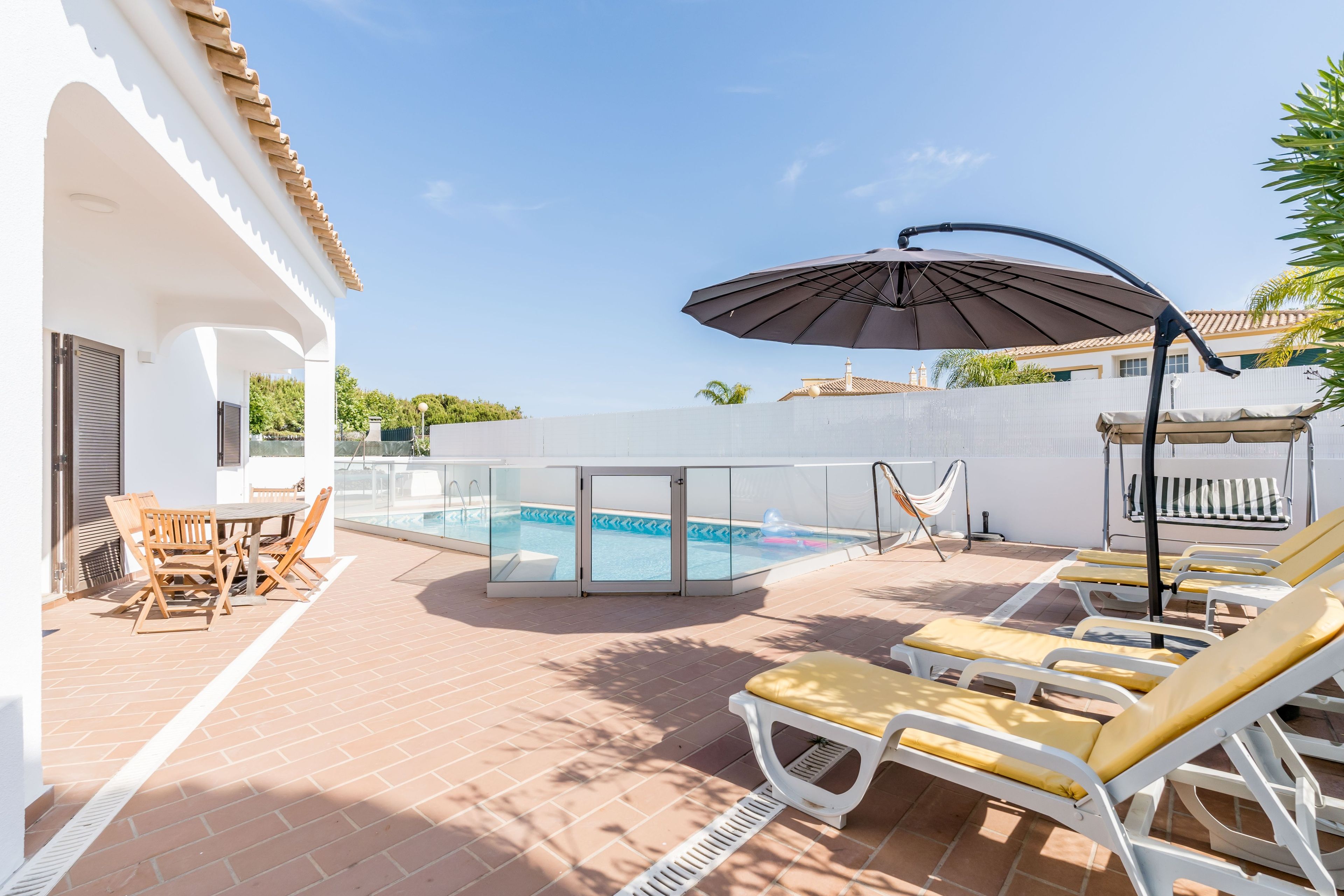 Ein Poolbereich mit Liegestühlen, einem Tisch und einem großen Sonnenschirm.