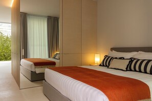 A hotel room with a large bed, a bedside table with a lamp, a mirror, and a view of greenery outside.