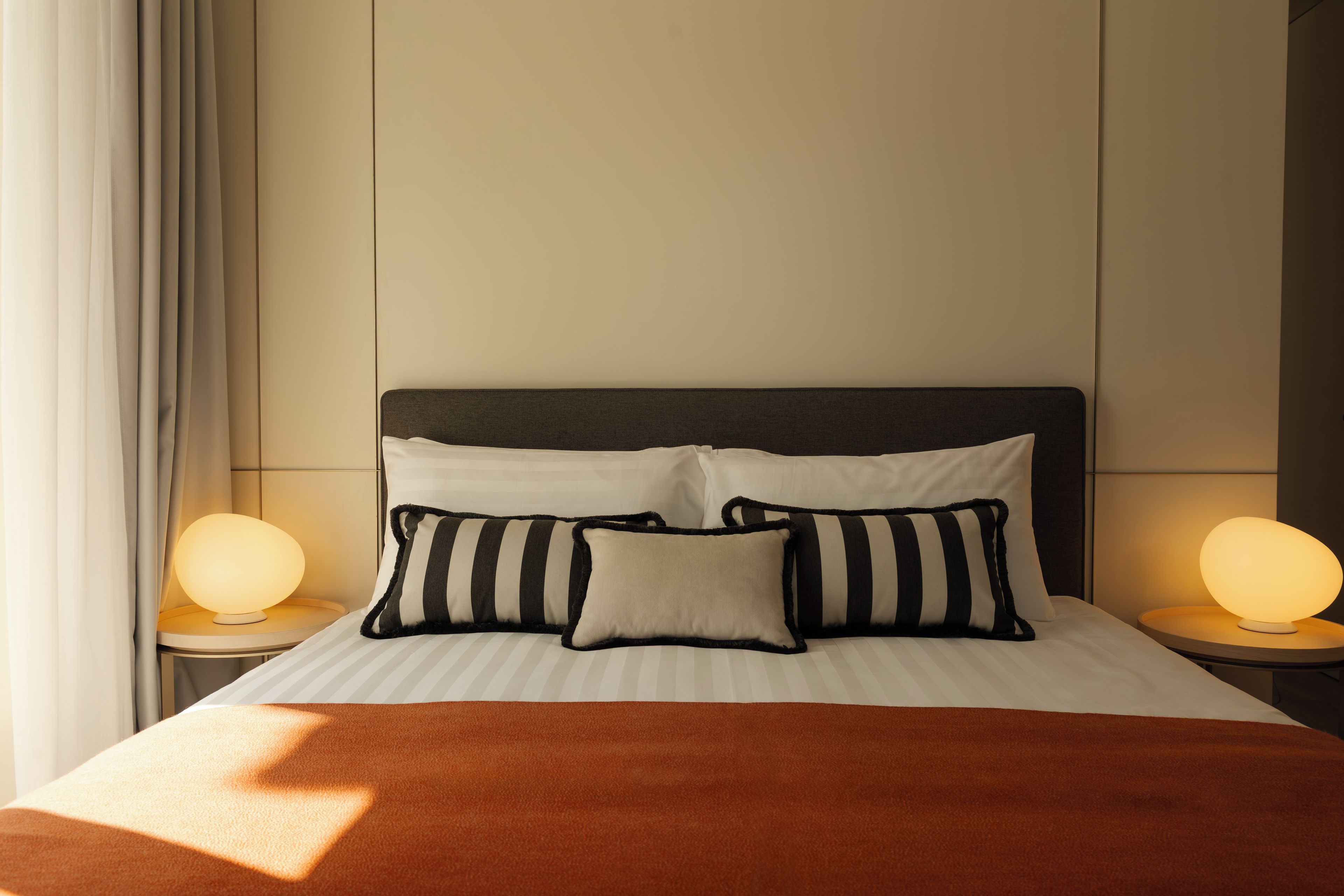 A neatly made bed with striped pillows and a brown blanket, flanked by two bedside lamps on matching nightstands.