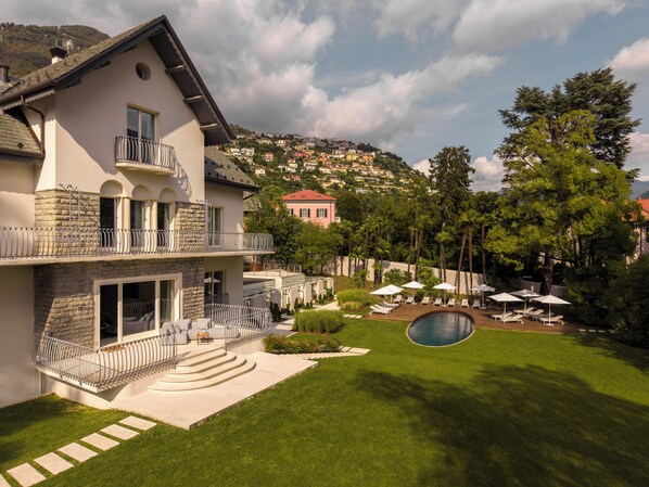 A two-story house with a swimming pool, outdoor seating, and a view of a hillside.