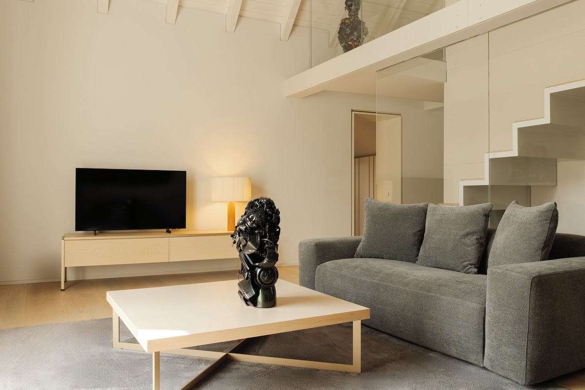 A modern living room with a flat-screen TV, a sculpture on a coffee table, and a grey sofa.