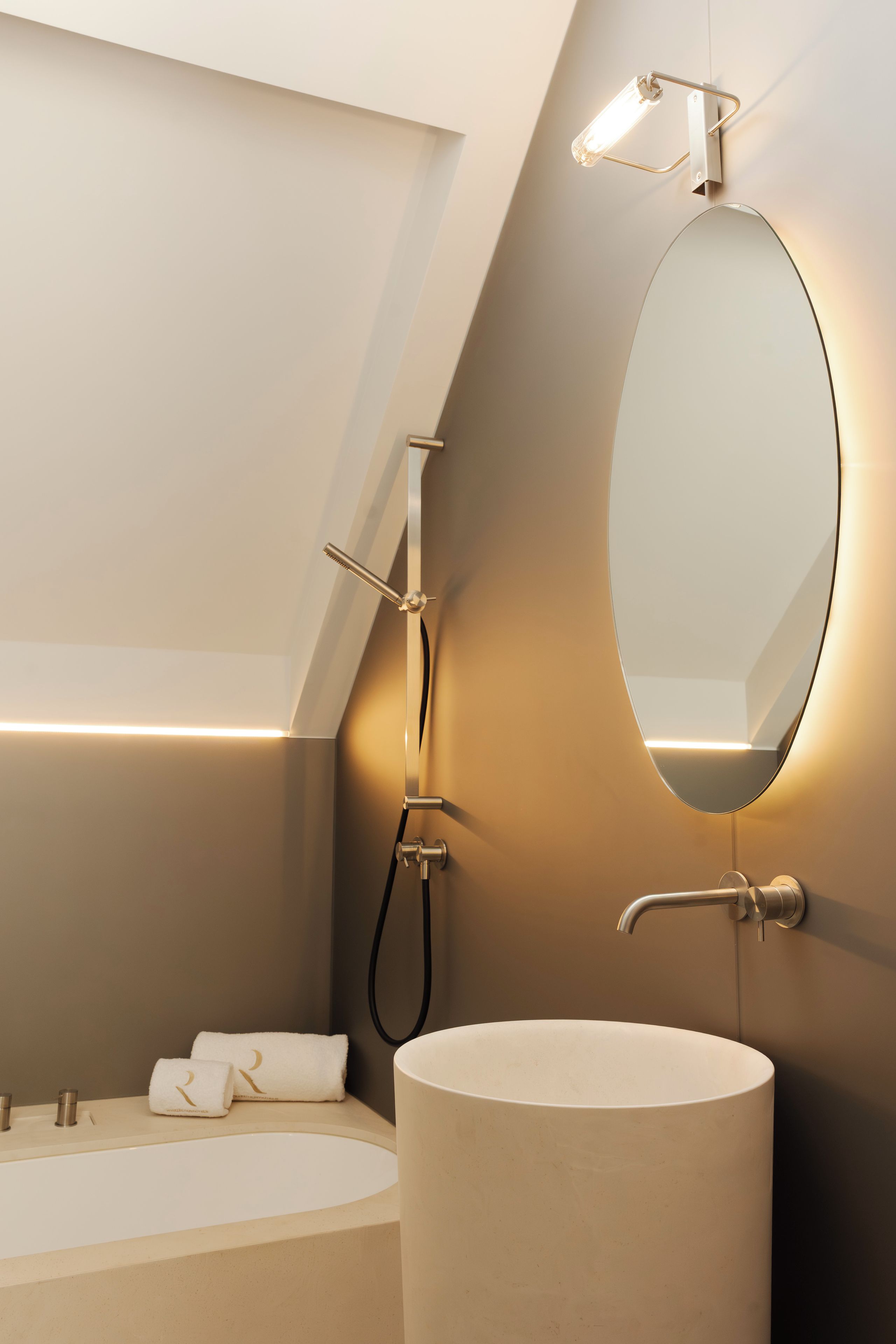 A modern bathroom with a skylight, a round mirror, and a bathtub.
