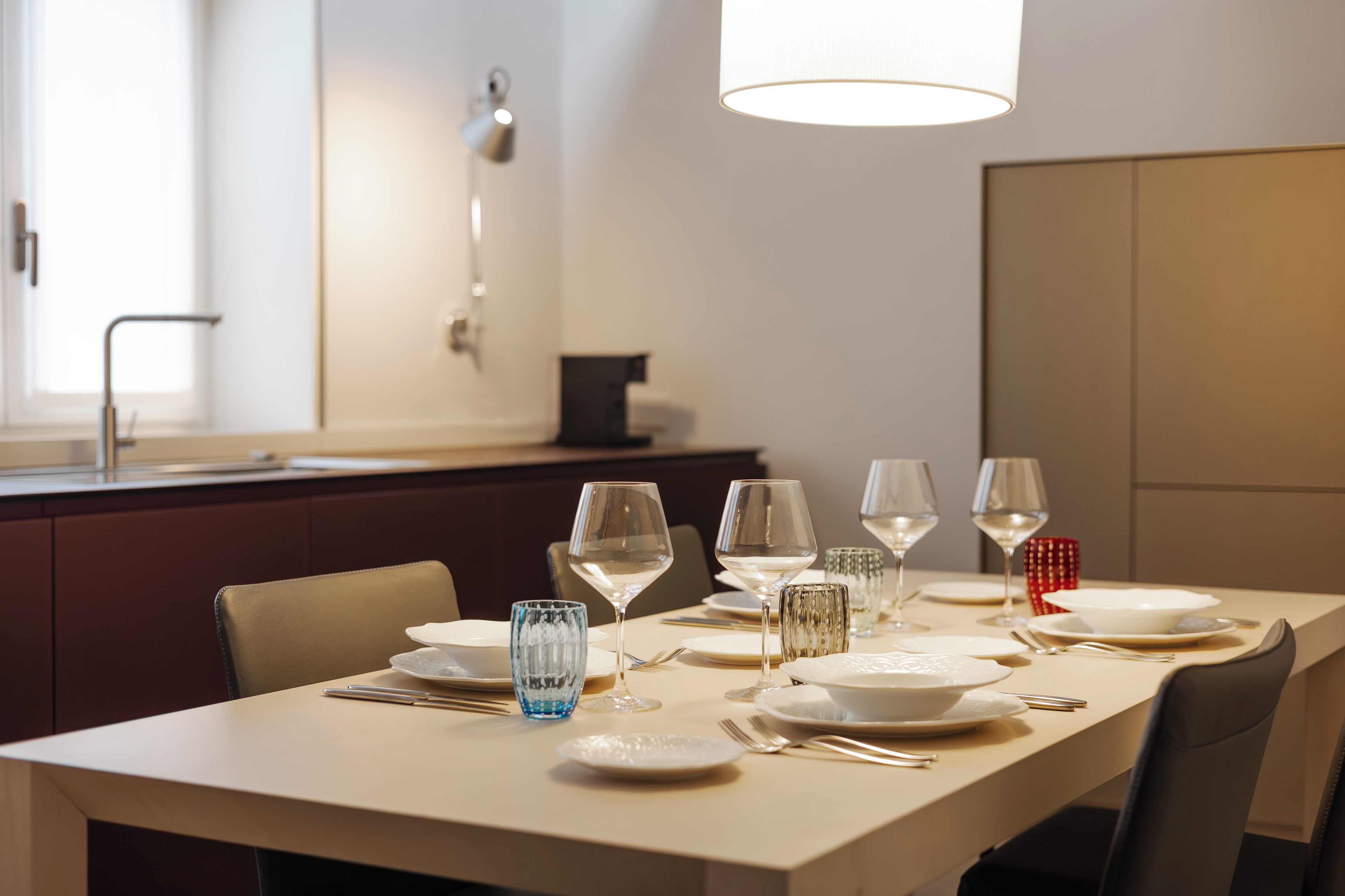 Una mesa de comedor dispuesta con platos, vasos y cubiertos, con una lámpara moderna encima.
