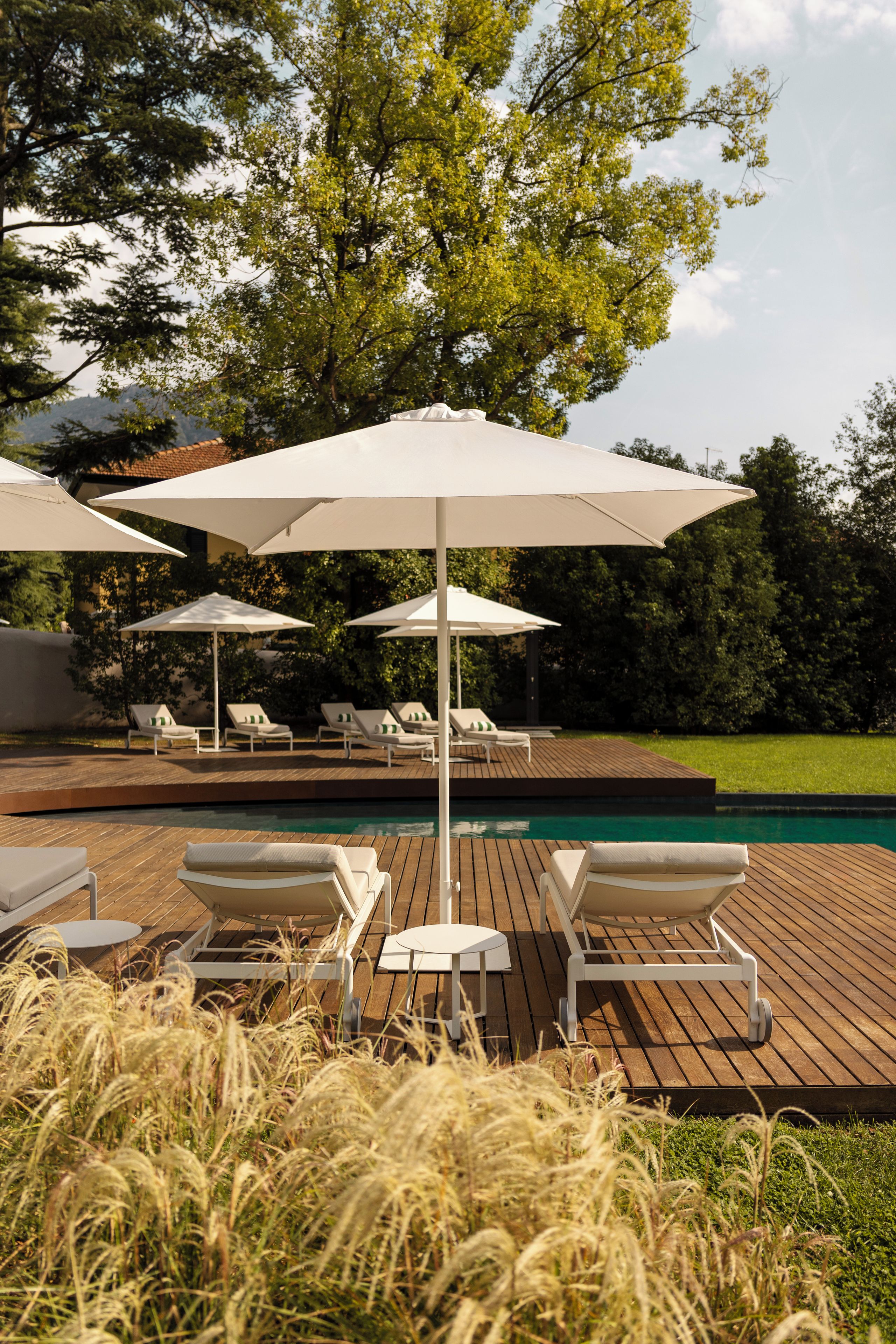 Zona junto a la piscina con cubierta de madera, sillas de descanso y sombrillas.