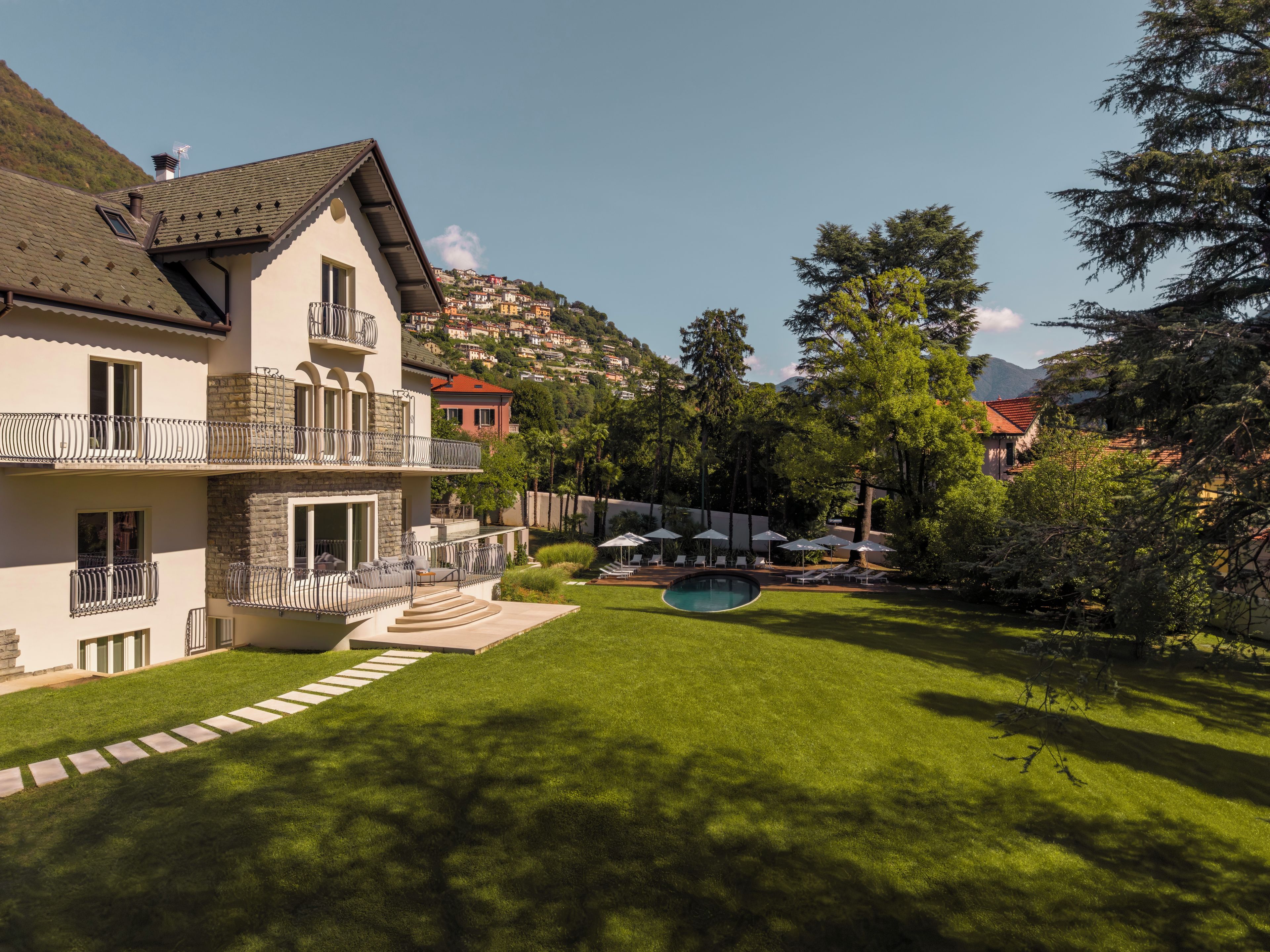 A two-story house with a swimming pool, a well-maintained lawn, and a view of a hillside community.