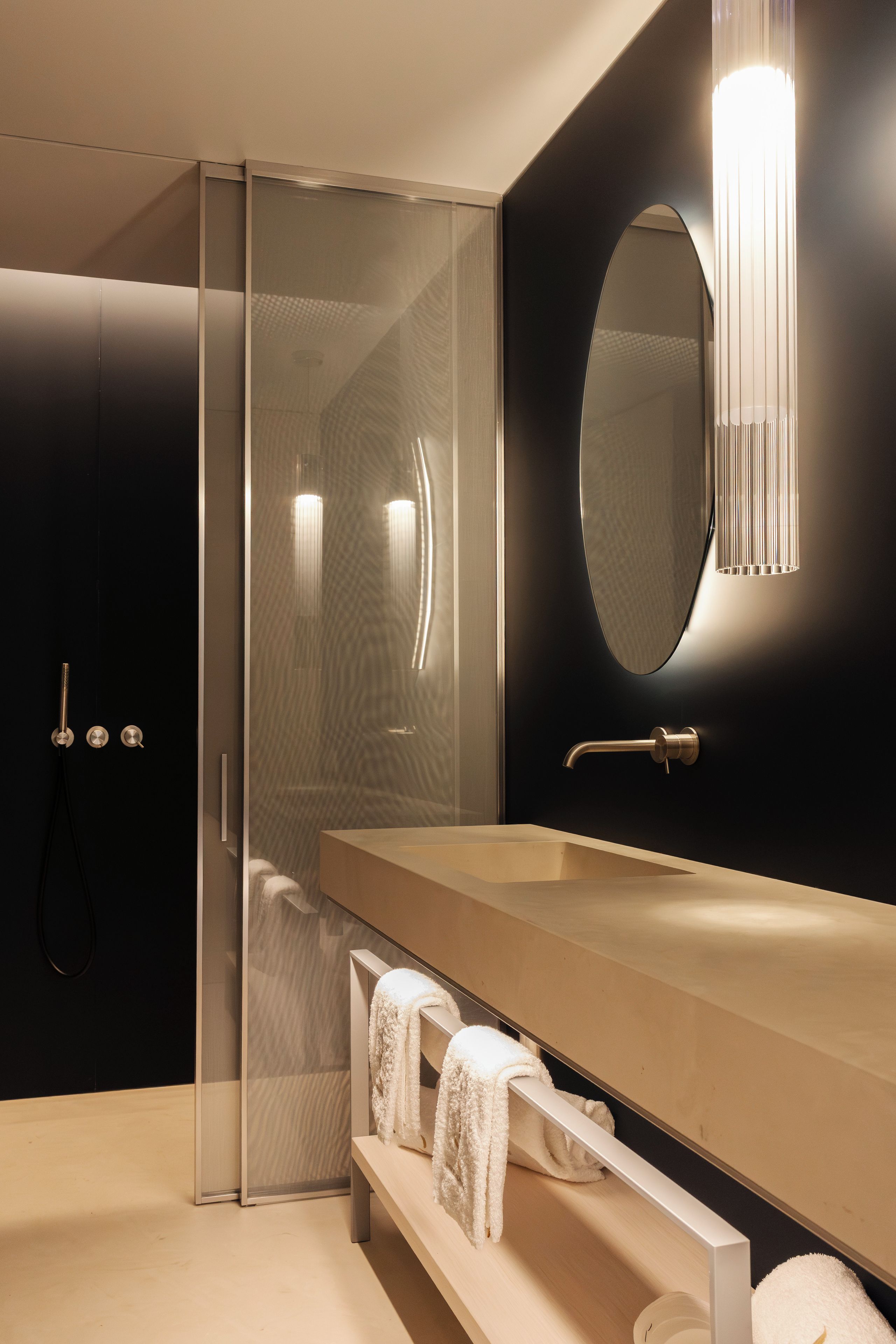 Un baño moderno con cabina de ducha de vidrio, tocador de madera con espejo y dos toallas en un estante.