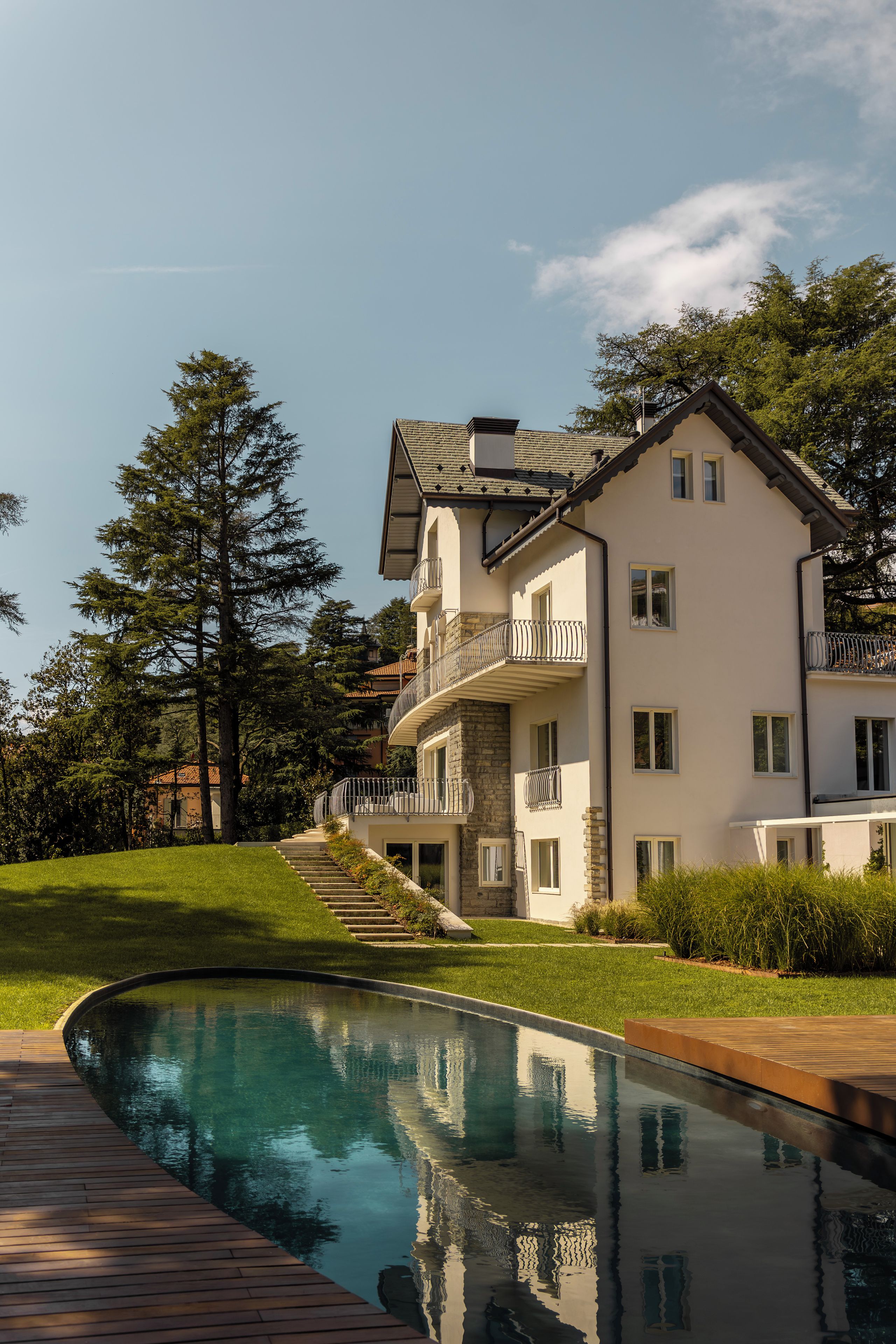 A two-story house with a swimming pool, surrounded by trees and a well-maintained lawn.
