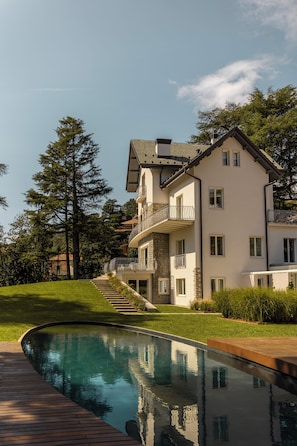 A two-story house with a swimming pool, surrounded by trees and a well-maintained lawn.