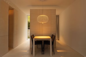 A modern dining area with a table and chairs, a pendant light, and a view of greenery outside.