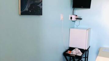 A room with a television mounted on the wall, a whiteboard, and a small table with a chair.