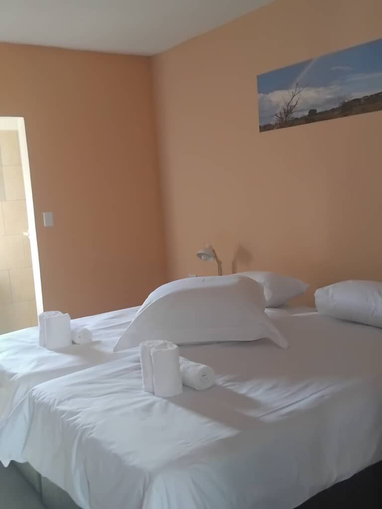A hotel room with a bed, pillows, and a painting on the wall.