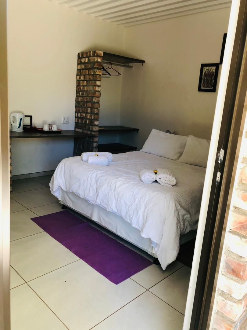 A hotel room with a bed, a brick pillar, a desk with a chair, and a purple rug.