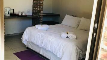 A hotel room with a bed, a brick pillar, a desk with a chair, and a purple rug.