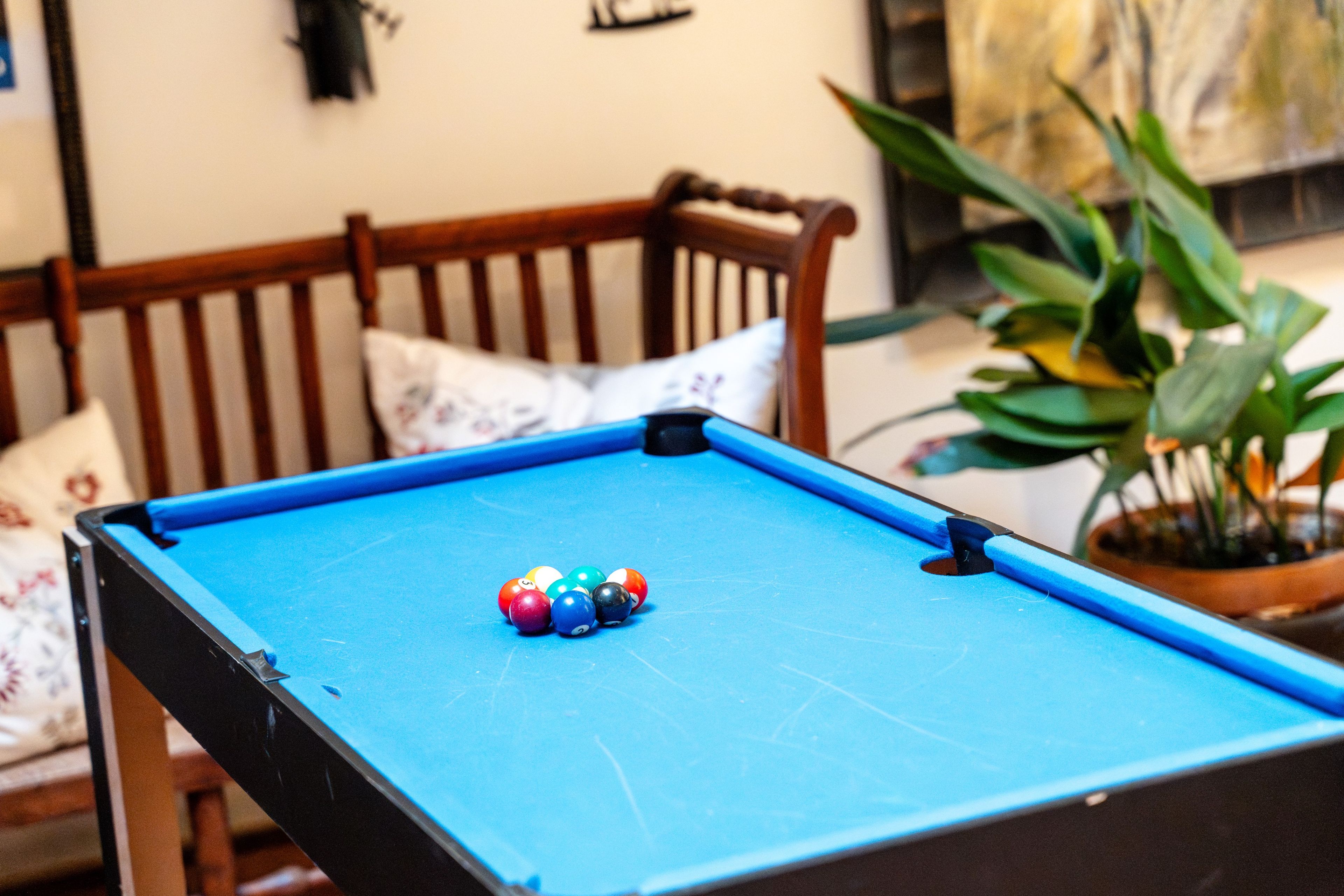 Una mesa de billar con bolas de billar en una habitación que tiene una silla de madera y una planta en maceta.