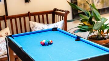 Una mesa de billar con bolas de billar en una habitación que tiene una silla de madera y una planta en maceta.