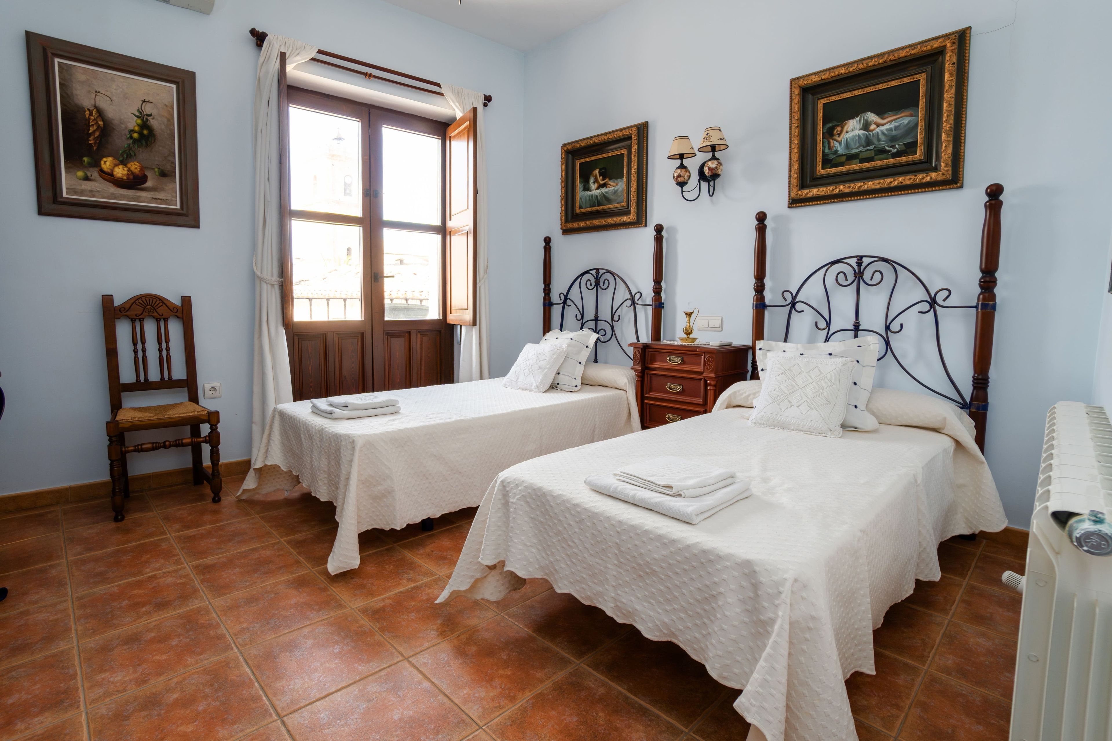 Un dormitorio con dos camas individuales, una silla de madera, una mesita de noche y un radiador.